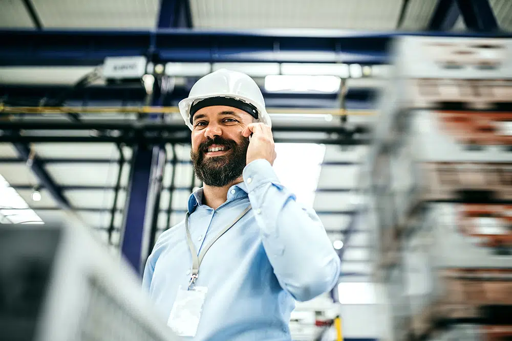 A portrait of a mature industrial man engineer with smartphone in a factory, making a phone call.